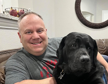 Image of David Votano sitting with his black lab